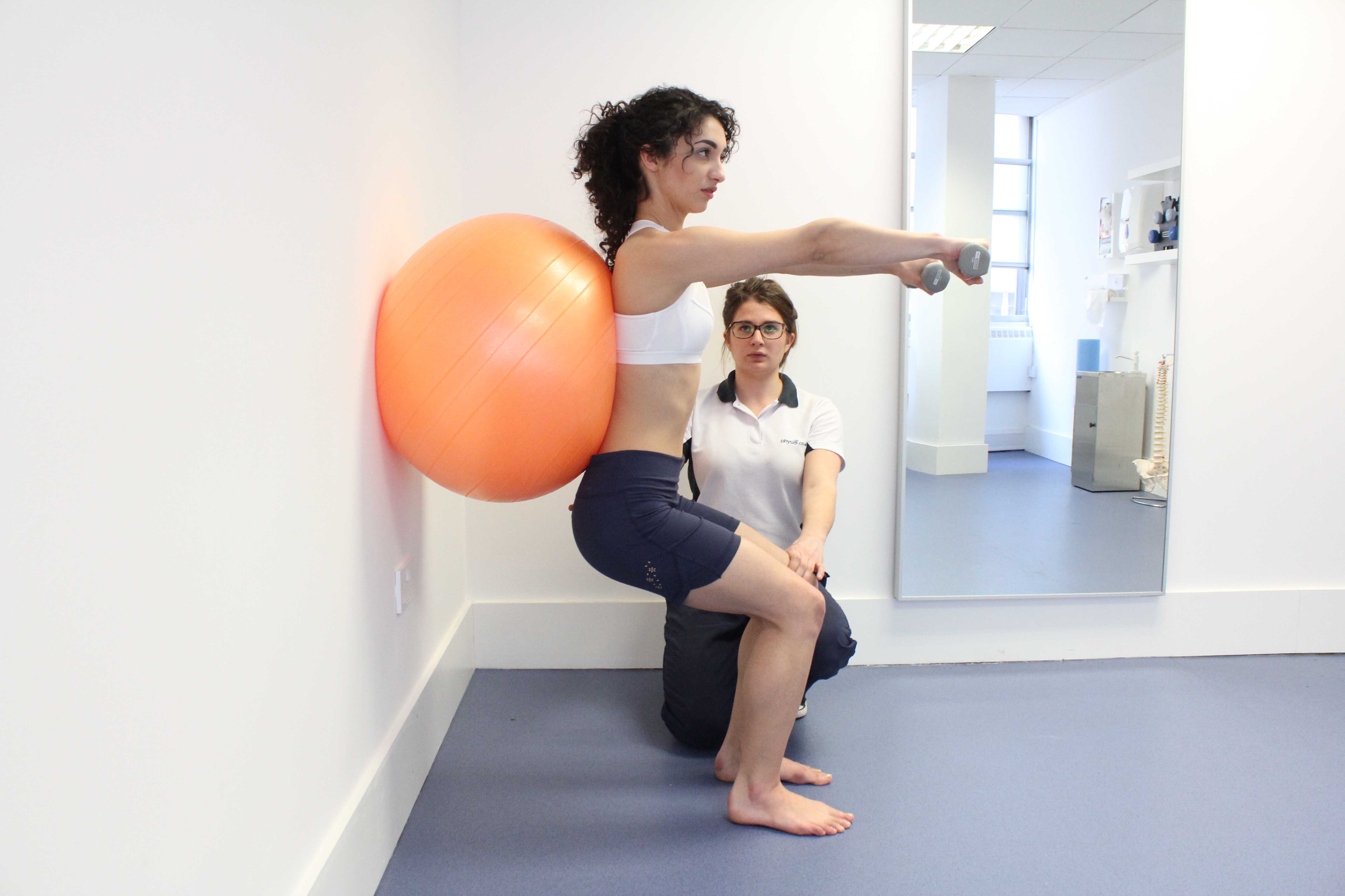 Leg strengthening exercises using squats and a gym ball with hand weights, under supervision of specialist MSK physiotherapist