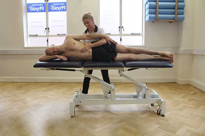 Customer receiving abdominal massage while laying on his side in Manchester Physio Clinic