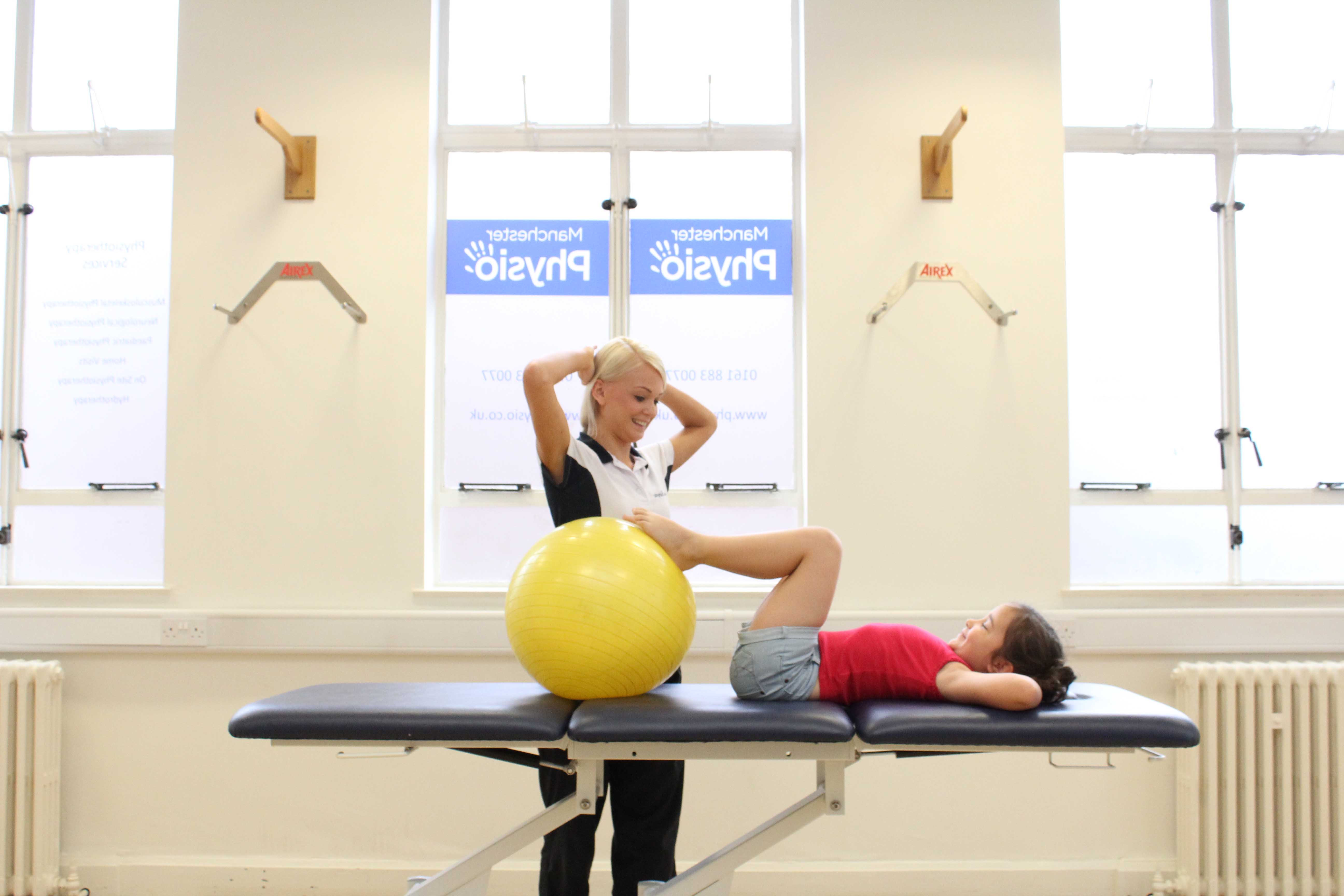 Specialist physiotherapist supervising lower limb stretching exercises using a gym ball