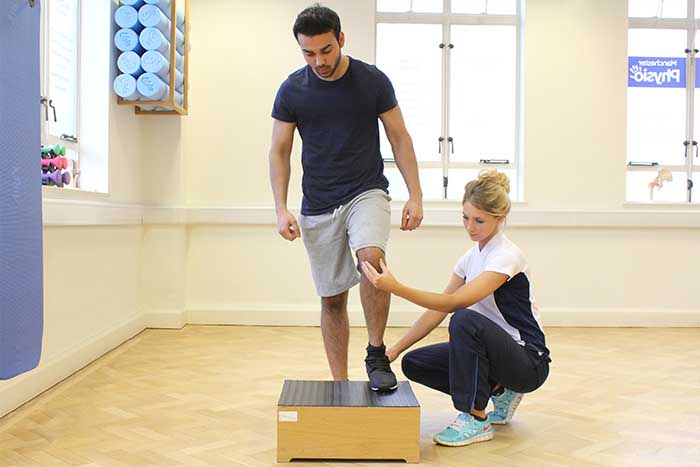Customer doing leg muscle stretches while using a standing block in Manchester Physio Clinic
